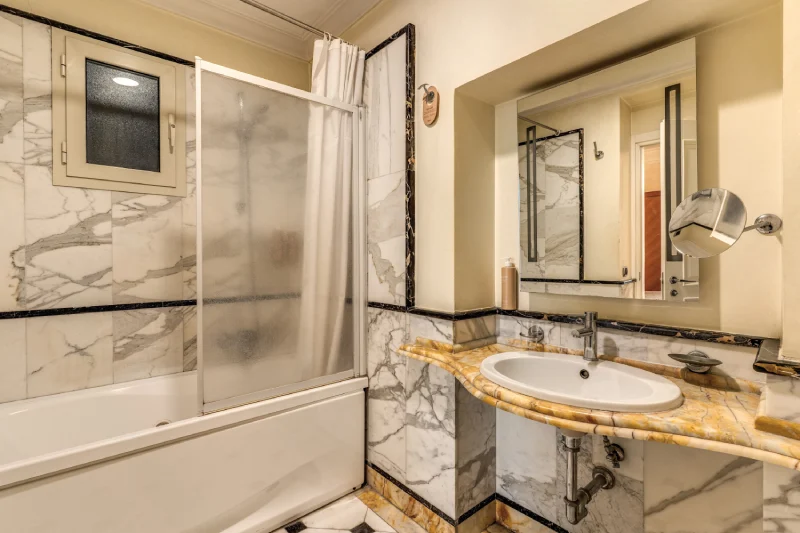 Bagno con vasca doccia, rivestimenti in marmo e lavabo in pietra, ambiente luminoso vicino Teatro dell’Opera Roma - Depandance Opera, BZAR hotels a Roma